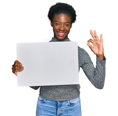 Poster - Young african american girl holding blank empty banner doing ok sign with fingers, smiling friendly gesturing excellent symbol