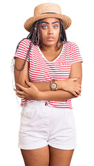 Sticker - Young african american woman with braids wearing summer hat shaking and freezing for winter cold with sad and shock expression on face