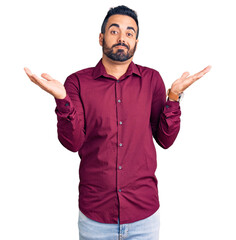 Canvas Print - Young hispanic man wearing casual clothes clueless and confused expression with arms and hands raised. doubt concept.