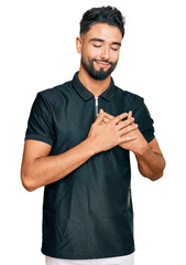 Canvas Print - Young man with beard wearing sportswear smiling with hands on chest with closed eyes and grateful gesture on face. health concept.