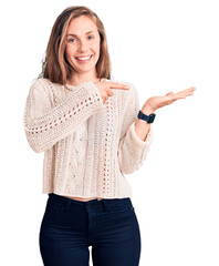 Poster - Young beautiful blonde woman wearing casual sweater amazed and smiling to the camera while presenting with hand and pointing with finger.