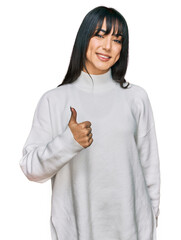 Sticker - Young brunette woman with bangs wearing casual turtleneck sweater doing happy thumbs up gesture with hand. approving expression looking at the camera showing success.