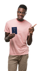 Poster - Young african american man holding german passport very happy pointing with hand and finger to the side