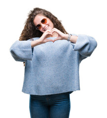 Poster - Beautiful brunette curly hair young girl wearing sunglasses over isolated background smiling in love showing heart symbol and shape with hands. Romantic concept.