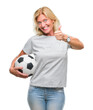 Middle age blonde woman holding soccer football ball over isolated background happy with big smile doing ok sign, thumb up with fingers, excellent sign