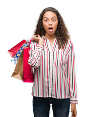 Poster - Young hispanic woman holding shopping bags scared in shock with a surprise face, afraid and excited with fear expression