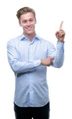 Poster - Young handsome blond man very happy pointing with hand and finger to the side