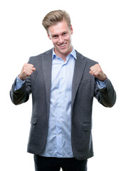 Canvas Print - Young handsome blond business man very happy and excited doing winner gesture with arms raised, smiling and screaming for success. Celebration concept.