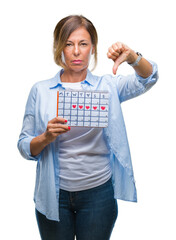 Sticker - Middle age senior hispanic woman holding menstruation calendar over isolated background with angry face, negative sign showing dislike with thumbs down, rejection concept