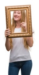 Sticker - Blonde teenager woman holding vintage frame art surprised with an idea or question pointing finger with happy face, number one