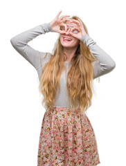 Poster - Blonde teenager woman wearing flowers skirt doing ok gesture like binoculars sticking tongue out, eyes looking through fingers. Crazy expression.