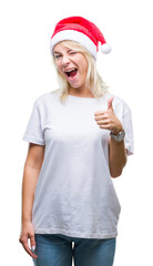 Sticker - Young beautiful blonde woman wearing christmas hat over isolated background doing happy thumbs up gesture with hand. Approving expression looking at the camera with showing success.