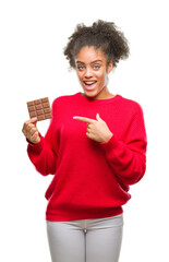 Canvas Print - Young afro american woman eating chocolate bar over isolated background very happy pointing with hand and finger