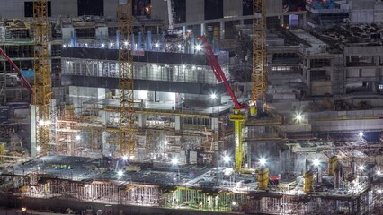 Wall Mural - Large construction site with many working cranes and workers in uniform night timelapse. Top aerial view of big development of residential and office district in Business bay, Dubai