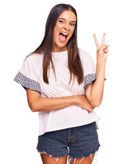 Wall Mural - Young hispanic woman wearing casual clothes smiling with happy face winking at the camera doing victory sign. number two.