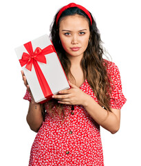 Canvas Print - Young hispanic girl holding gift relaxed with serious expression on face. simple and natural looking at the camera.