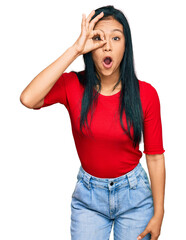 Wall Mural - Beautiful hispanic woman wearing casual clothes doing ok gesture shocked with surprised face, eye looking through fingers. unbelieving expression.