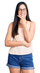 Sticker - Young beautiful caucasian woman wearing casual clothes and glasses looking confident at the camera smiling with crossed arms and hand raised on chin. thinking positive.