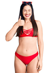 Canvas Print - Young beautiful caucasian woman wearing bikini doing happy thumbs up gesture with hand. approving expression looking at the camera showing success.