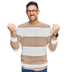 Sticker - Handsome man with beard wearing casual clothes and glasses very happy and excited doing winner gesture with arms raised, smiling and screaming for success. celebration concept.