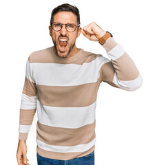 Canvas Print - Handsome man with beard wearing casual clothes and glasses angry and mad raising fist frustrated and furious while shouting with anger. rage and aggressive concept.