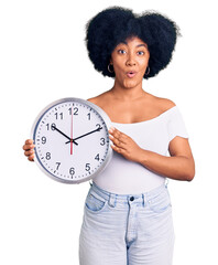 Canvas Print - Young african american girl holding big clock scared and amazed with open mouth for surprise, disbelief face