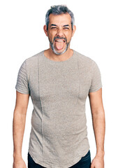 Canvas Print - Middle age hispanic with grey hair wearing casual grey t shirt sticking tongue out happy with funny expression. emotion concept.