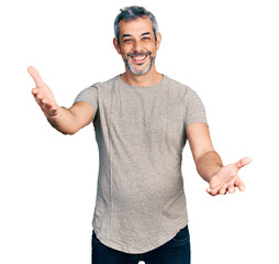 Poster - Middle age hispanic with grey hair wearing casual grey t shirt looking at the camera smiling with open arms for hug. cheerful expression embracing happiness.