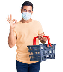 Sticker - Young hispanic man wearing shopping basket and medical mask doing ok sign with fingers, smiling friendly gesturing excellent symbol