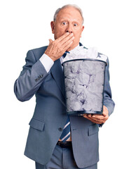 Wall Mural - Senior handsome grey-haired man holding paper bin with crumpled document covering mouth with hand, shocked and afraid for mistake. surprised expression