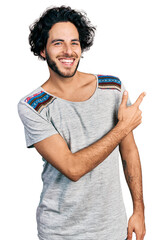 Sticker - Young hispanic man wearing casual t shirt cheerful with a smile of face pointing with hand and finger up to the side with happy and natural expression on face