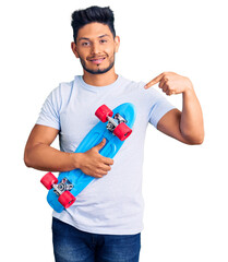 Wall Mural - Handsome latin american young man holding skate pointing finger to one self smiling happy and proud