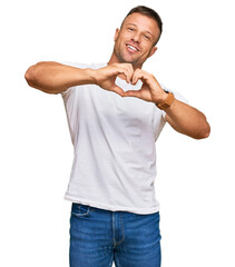 Canvas Print - Handsome muscle man wearing casual white tshirt smiling in love doing heart symbol shape with hands. romantic concept.