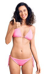 Sticker - Young beautiful hispanic woman wearing bikini doing happy thumbs up gesture with hand. approving expression looking at the camera showing success.