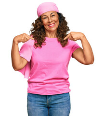 Canvas Print - Middle age hispanic woman wearing breast cancer support pink scarf looking confident with smile on face, pointing oneself with fingers proud and happy.