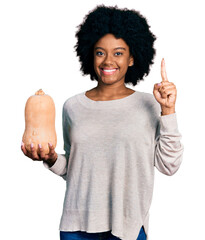 Canvas Print - Young african american woman holding healthy fresh pumpkin smiling with an idea or question pointing finger with happy face, number one