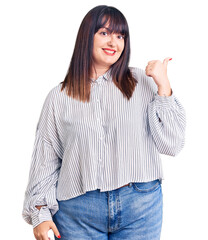 Poster - Young plus size woman wearing casual clothes smiling with happy face looking and pointing to the side with thumb up.