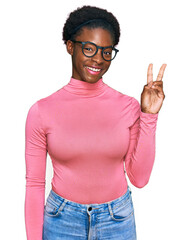 Wall Mural - Young african american girl wearing casual clothes and glasses showing and pointing up with fingers number two while smiling confident and happy.