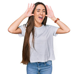 Poster - Young hispanic girl wearing casual white t shirt smiling cheerful playing peek a boo with hands showing face. surprised and exited