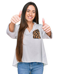 Canvas Print - Young hispanic girl wearing casual clothes approving doing positive gesture with hand, thumbs up smiling and happy for success. winner gesture.