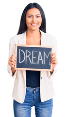 Poster - Young beautiful latin girl holding blackboard with dream word looking positive and happy standing and smiling with a confident smile showing teeth