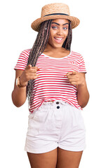 Sticker - Young african american woman with braids wearing summer hat pointing fingers to camera with happy and funny face. good energy and vibes.