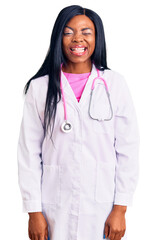 Wall Mural - Young african american woman wearing doctor stethoscope winking looking at the camera with sexy expression, cheerful and happy face.