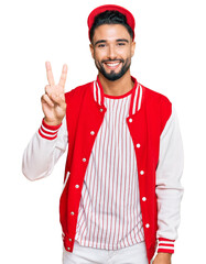 Canvas Print - Young man with beard wearing baseball uniform showing and pointing up with fingers number two while smiling confident and happy.