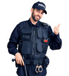 © Krakenimages.com - Young handsome man with beard wearing police uniform smiling with happy face looking and pointing to the side with thumb up.