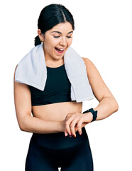 Wall Mural - Young brunette woman with blue eyes wearing gym clothes using smart watch celebrating crazy and amazed for success with open eyes screaming excited.