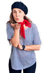 Sticker - Young beautiful blonde woman wearing french beret and striped t-shirt looking at the camera blowing a kiss with hand on air being lovely and sexy. love expression.