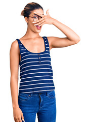 Sticker - Young beautiful woman wearing casual clothes and glasses peeking in shock covering face and eyes with hand, looking through fingers with embarrassed expression.