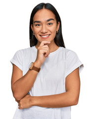 Wall Mural - Young asian woman wearing casual white t shirt looking confident at the camera with smile with crossed arms and hand raised on chin. thinking positive.