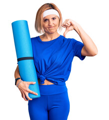 Poster - Young blonde woman holding yoga mat with angry face, negative sign showing dislike with thumbs down, rejection concept